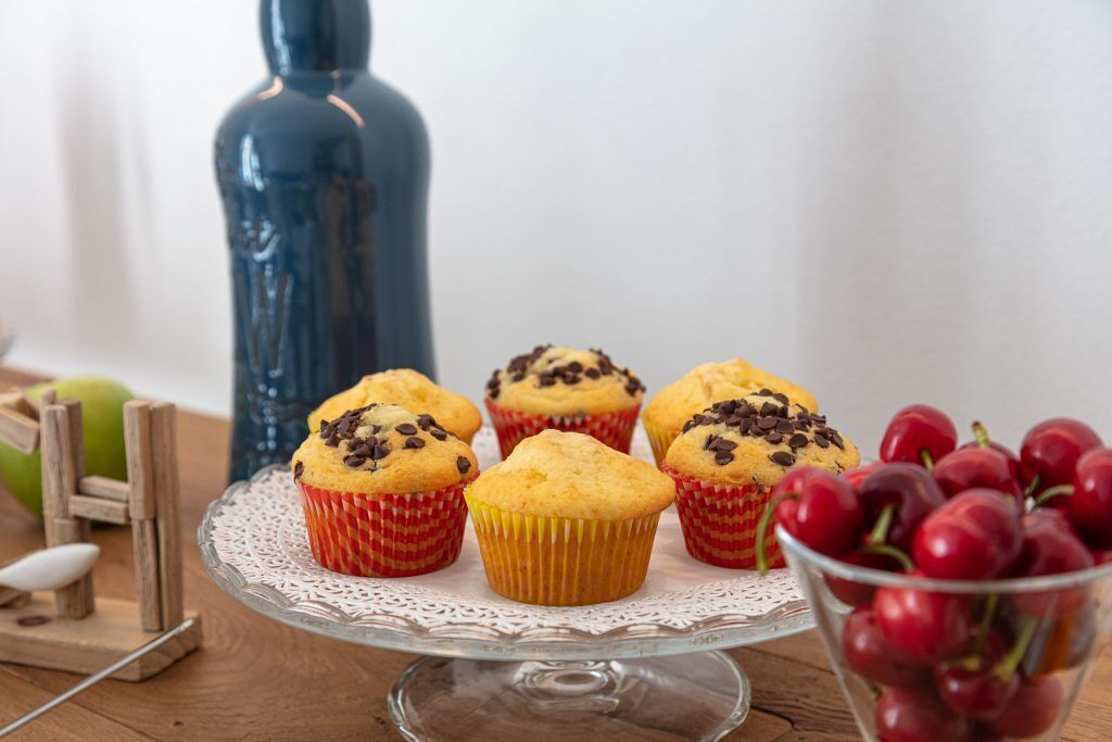 Une table sur laquelle se trouve un présentoir à gâteaux en verre, avec des muffins et un bol de cerises.