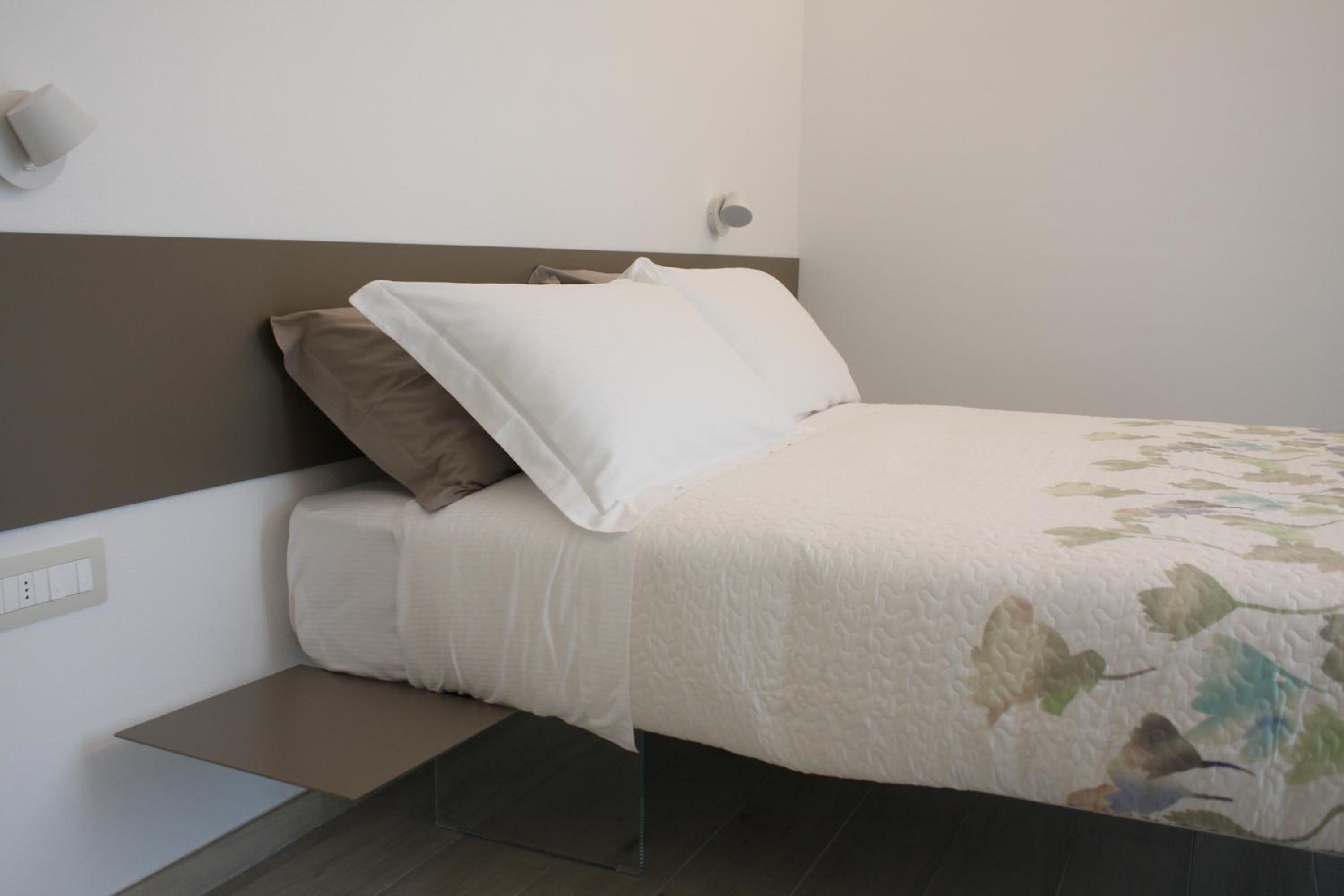A neatly made bed with a floral-patterned bedspread, a headboard, and a bedside table with a lamp.