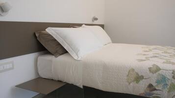 A neatly made bed with a floral-patterned bedspread, a headboard, and a bedside table with a lamp.