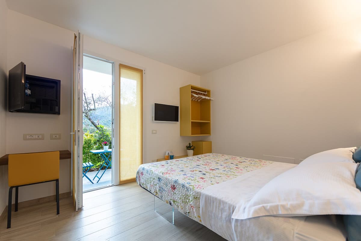 Une chambre à coucher avec un lit, un téléviseur fixé au mur, une petite table sur laquelle est posée une plante en pot et une chaise.