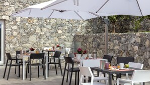 Een terras met stenen muren, tafels, stoelen en parasols.