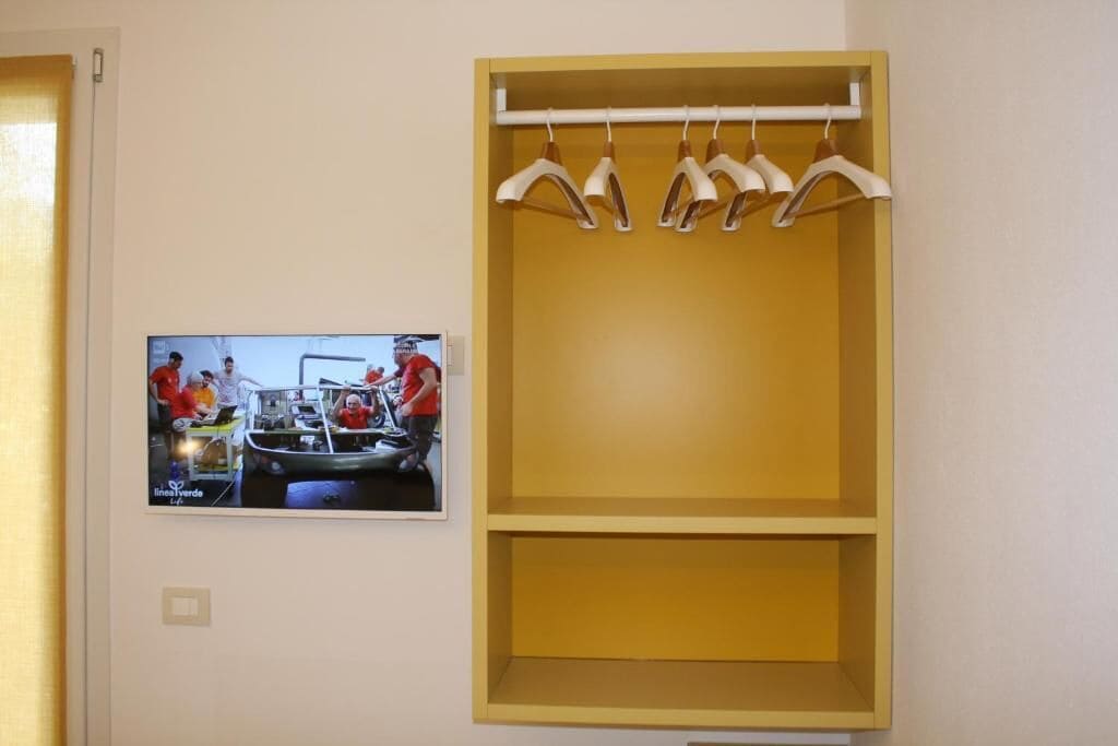 A room with a yellow wardrobe and a television displaying a program.