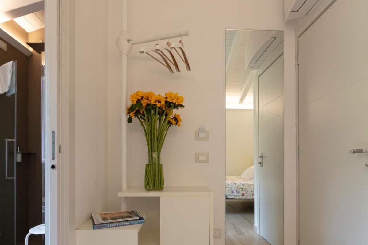 Un couloir moderne et minimaliste, avec un bureau blanc, un vase de fleurs et un miroir accroché au mur.