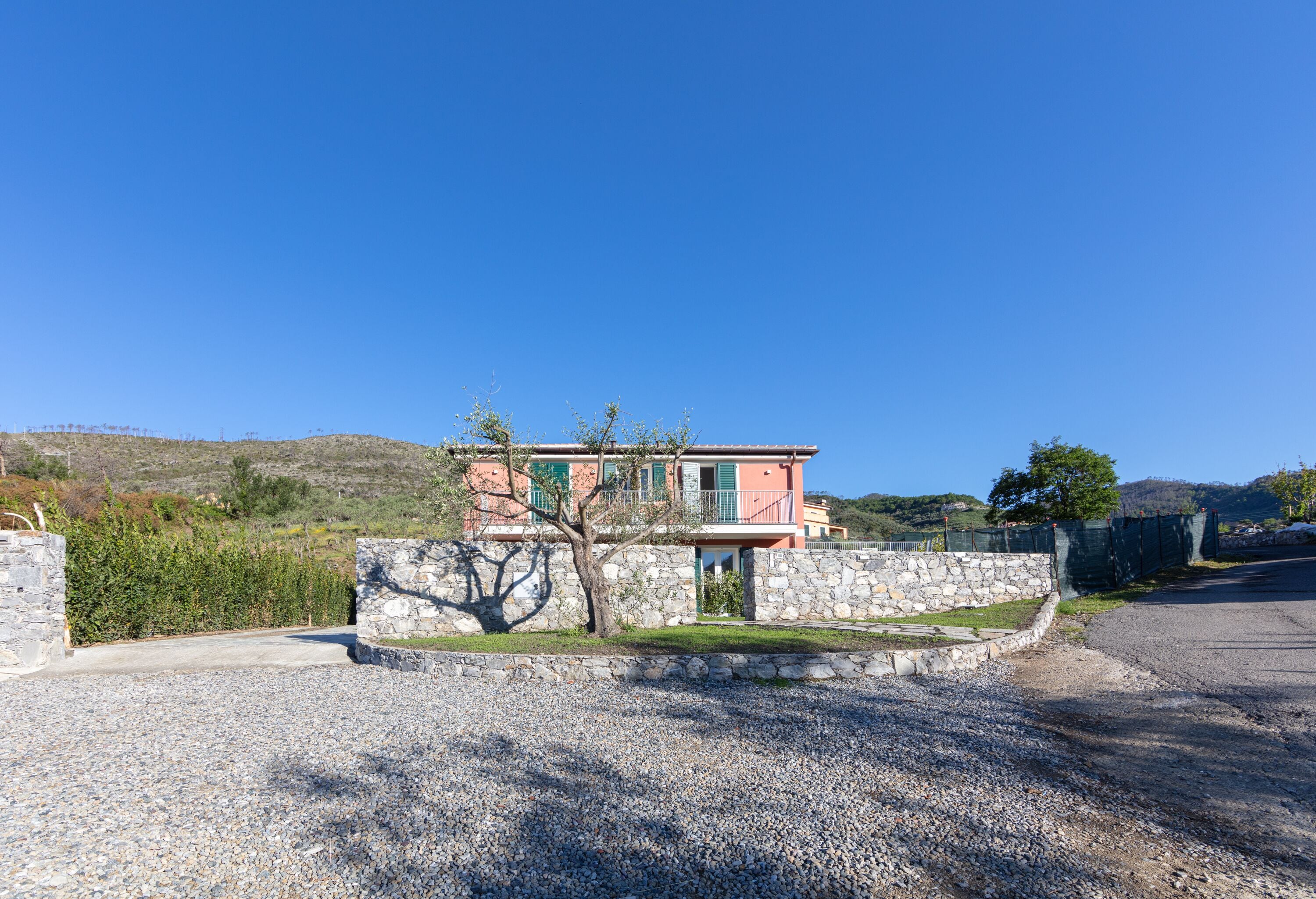 A modern house with a stone wall, a gravel driveway, and a clear blue sky.