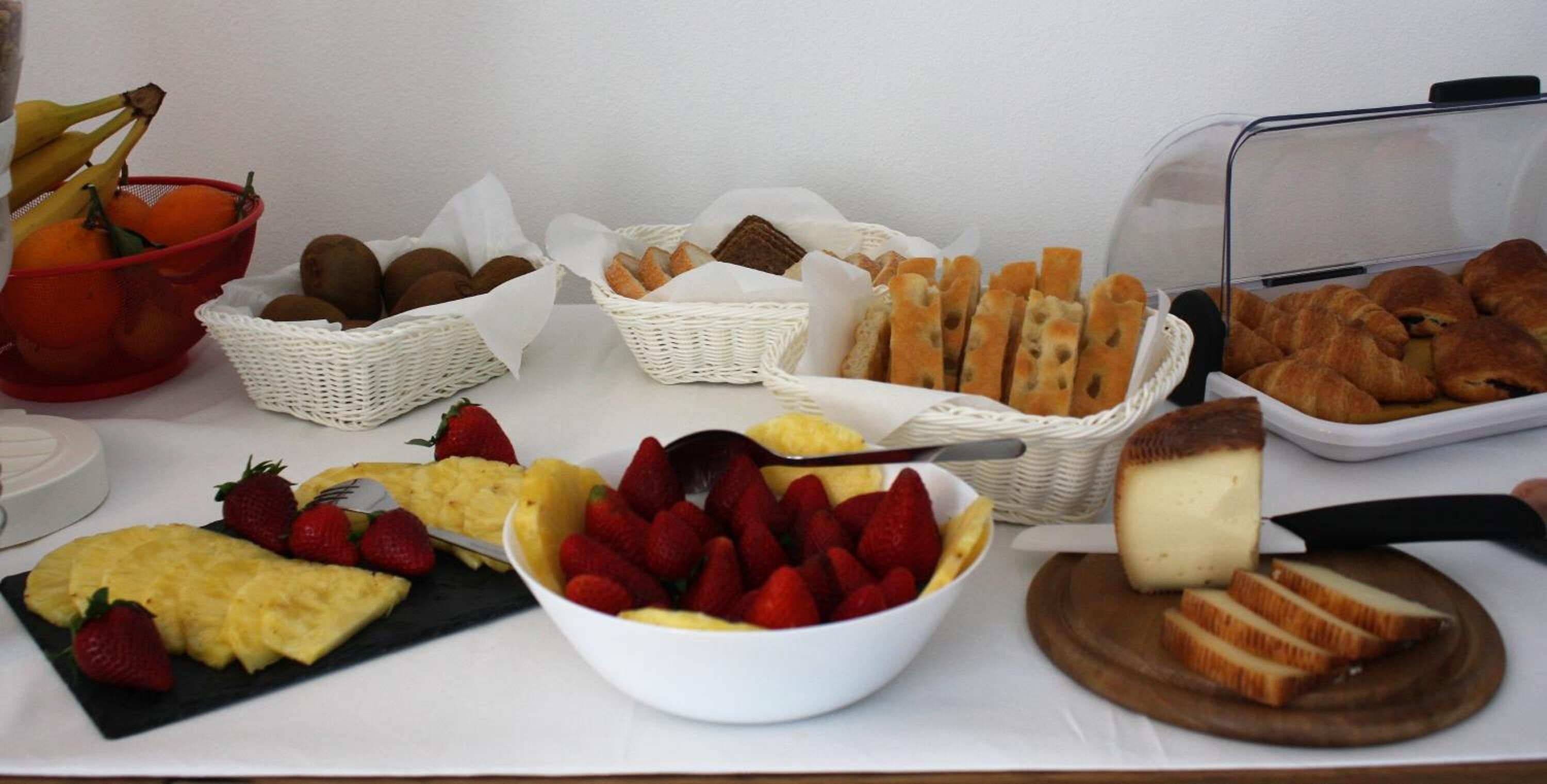 A buffet table with various food items including bread, pastries, fruits, and cheese.