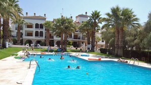 Una piscina con múltiples carriles, rodeada de palmeras y un edificio grande con balcones.