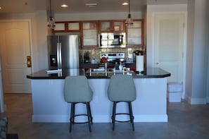 A modern kitchen with a central island, stainless steel appliances, and two bar stools.