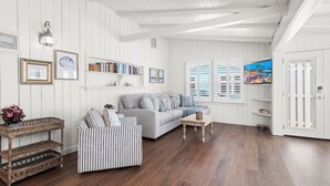 Una sala de estar con un sofá gris, un sillón a rayas, suelo de madera, paredes blancas y una estantería.