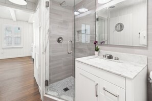 A modern bathroom with a glass-enclosed shower, a marble sink, and a large mirror. - Cottage Across The Street From #1 Beach (Siesta Key)