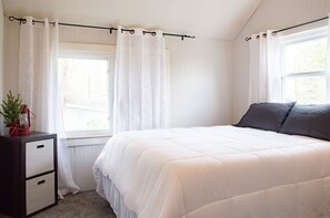 Quarto com uma cama, mesa de cabeceira, janela com cortinas e uma pequena planta na mesa de cabeceira.