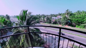A balcony with a view of a road, palm trees, and residential buildings. - Rachana Palace (Mangaluru)
