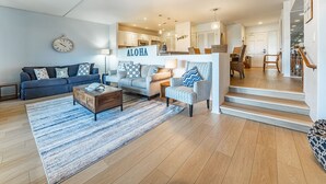 Una sala de estar moderna con sofá, sillones y una mesa de centro. Se ve una escalera que sube a otro nivel.