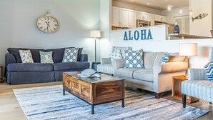 Una sala de estar con dos sofás, una mesa de centro y una zona de cocina con un letrero que dice "ALOHA".