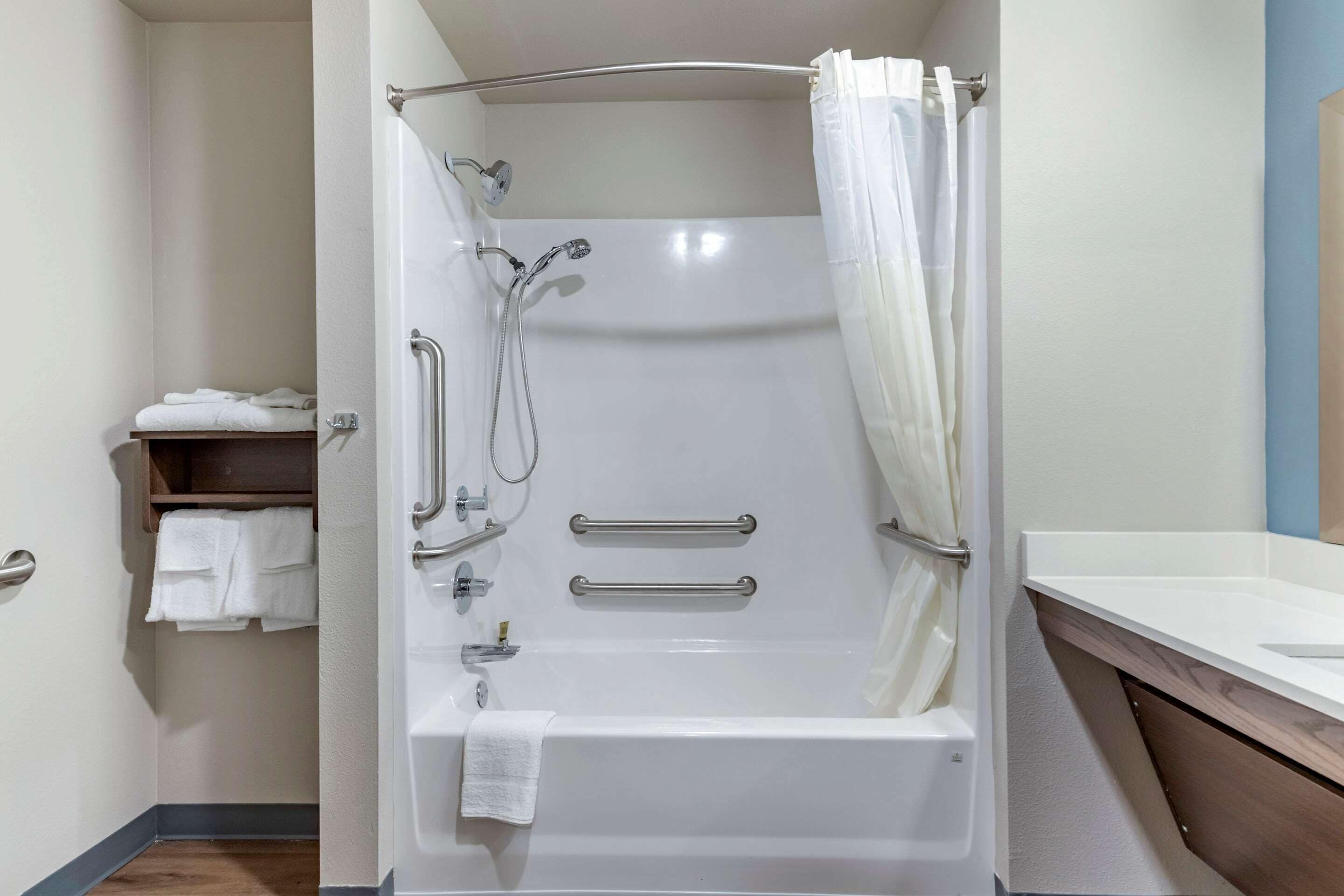 A modern bathroom with a walk-in shower, grab bars, and a towel rack.
