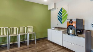 Un área de espera con cuatro sillas blancas, una máquina de café y un armario blanco.