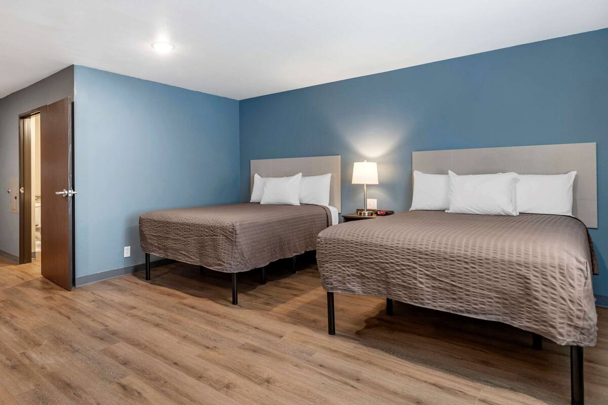 A hotel room with two beds, a door, and a nightstand with a lamp.