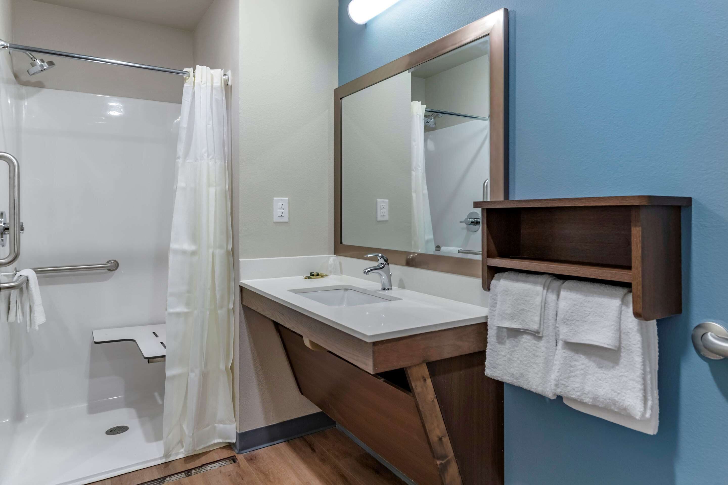 A bathroom with a shower, a sink, a mirror, and a towel rack.