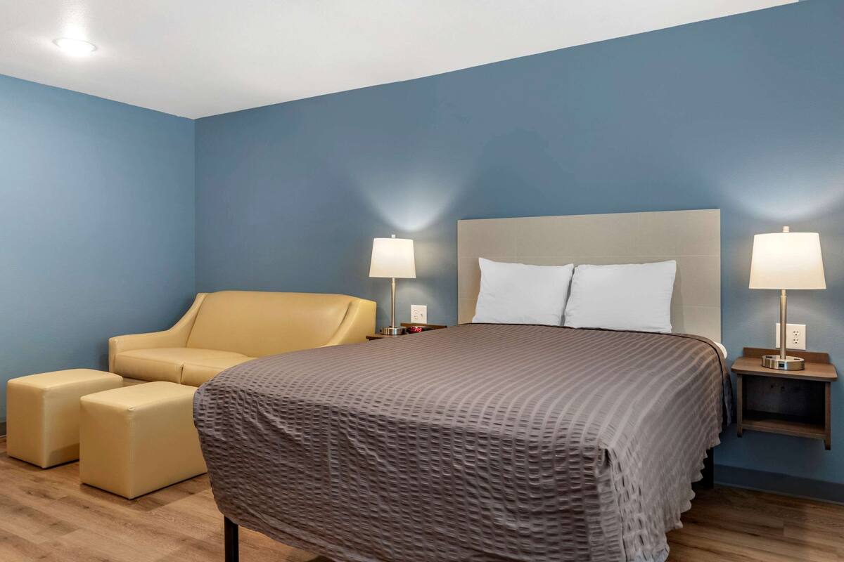 A hotel room with a bed, two bedside tables with lamps, a sofa, and two ottomans.