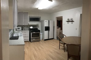 Enjoy meals at the dining table with two chairs, and access a kitchen with a stainless steel oven, microwave, and refrigerator.