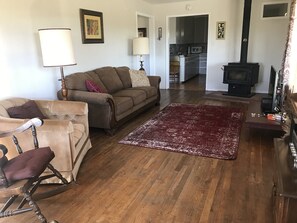A living room with a sofa, armchair, and a red rug. There is a kitchen in the background with a stove and cabinets. - Hillside Cottage:  Restful, quiet setting
Coconino County Permit # STR-25-0566 (Flagstaff)