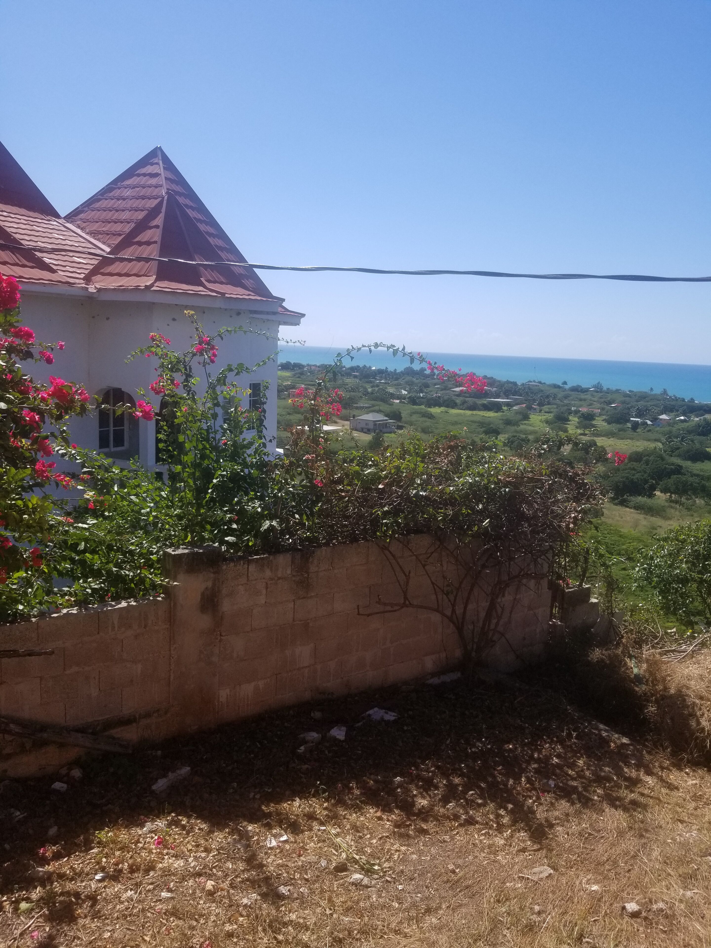 A white building with a red roof, surrounded by greenery and a clear view of the ocean.
