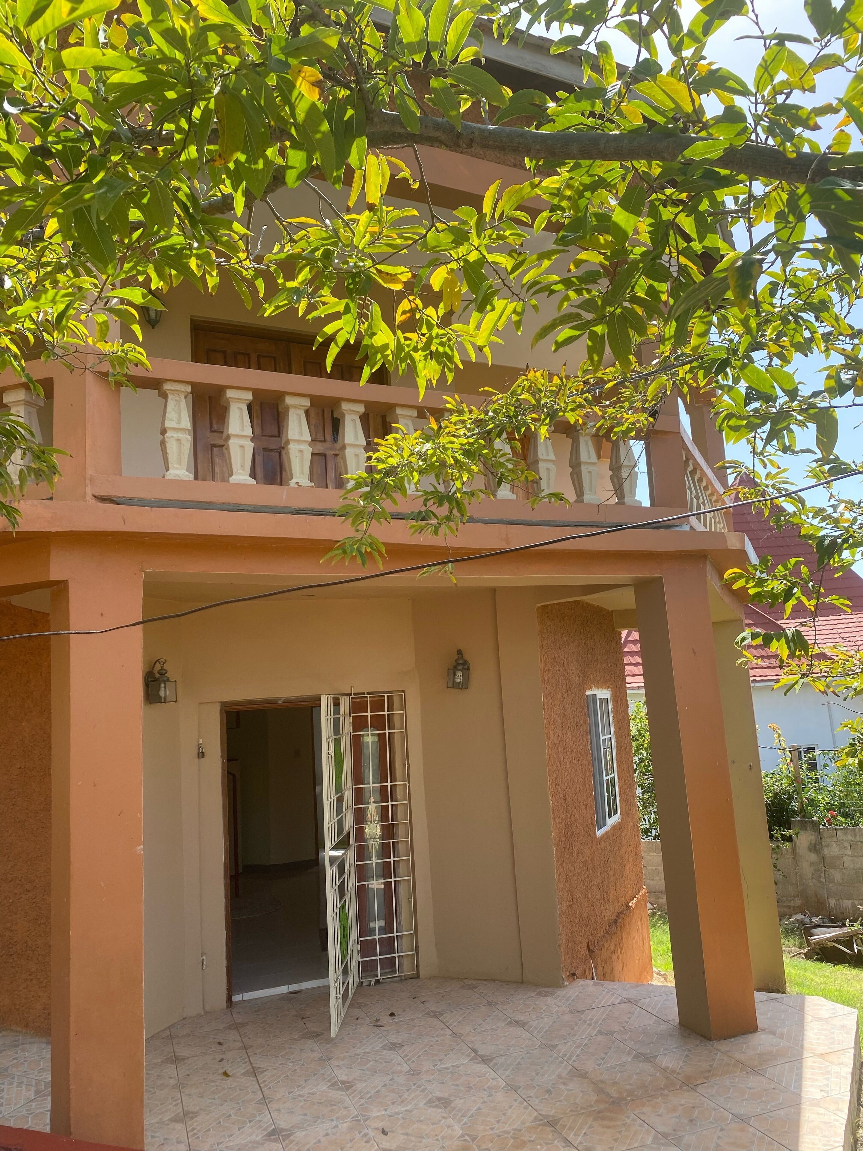 Un bâtiment à deux étages doté d’un balcon, d’une entrée fermée par un portail et d’une terrasse carrelée.