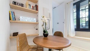 A room with a round wooden table, two wicker chairs, a potted orchid, and shelves with books and a motivational sign. - Apartamentos Madrid Rio (Madrid)