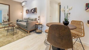 A modern living room with a sofa, a round table, and a chair. There is a painting on the wall and a vase with flowers. - Apartamentos Madrid Rio (Madrid)