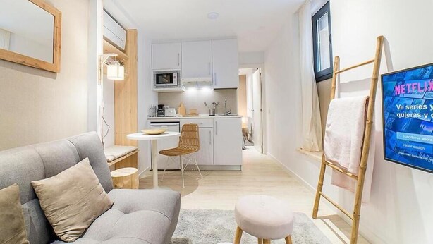 A modern living room with a grey sofa, a small round table, and a TV mounted on the wall. - Apartamentos Madrid Rio (Madrid)
