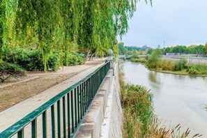 A riverside walkway with a metal railing, trees, and a bridge in the background. - Apartamentos Madrid Rio (Madrid)