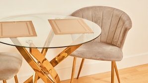 A round glass table with two woven placemats, a cushioned chair with a high back, and a golden metal base. - Modern Leeds City Apartment (Leeds)