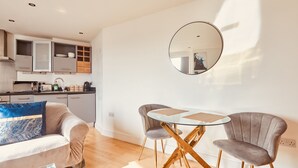 A modern living room with a sofa, two armchairs, a glass coffee table, and a round mirror on the wall. - Modern Leeds City Apartment (Leeds)