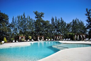 En swimmingpool med solstolar och trälusthus, omgiven av höga träd.