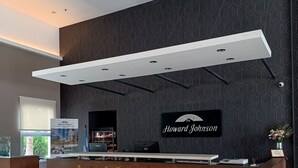 Un espace d’accueil avec un mur à motifs sombres, une enseigne indiquant « Howard Johnson », un comptoir d’accueil moderne et une grande fenêtre offrant une vue dégagée.