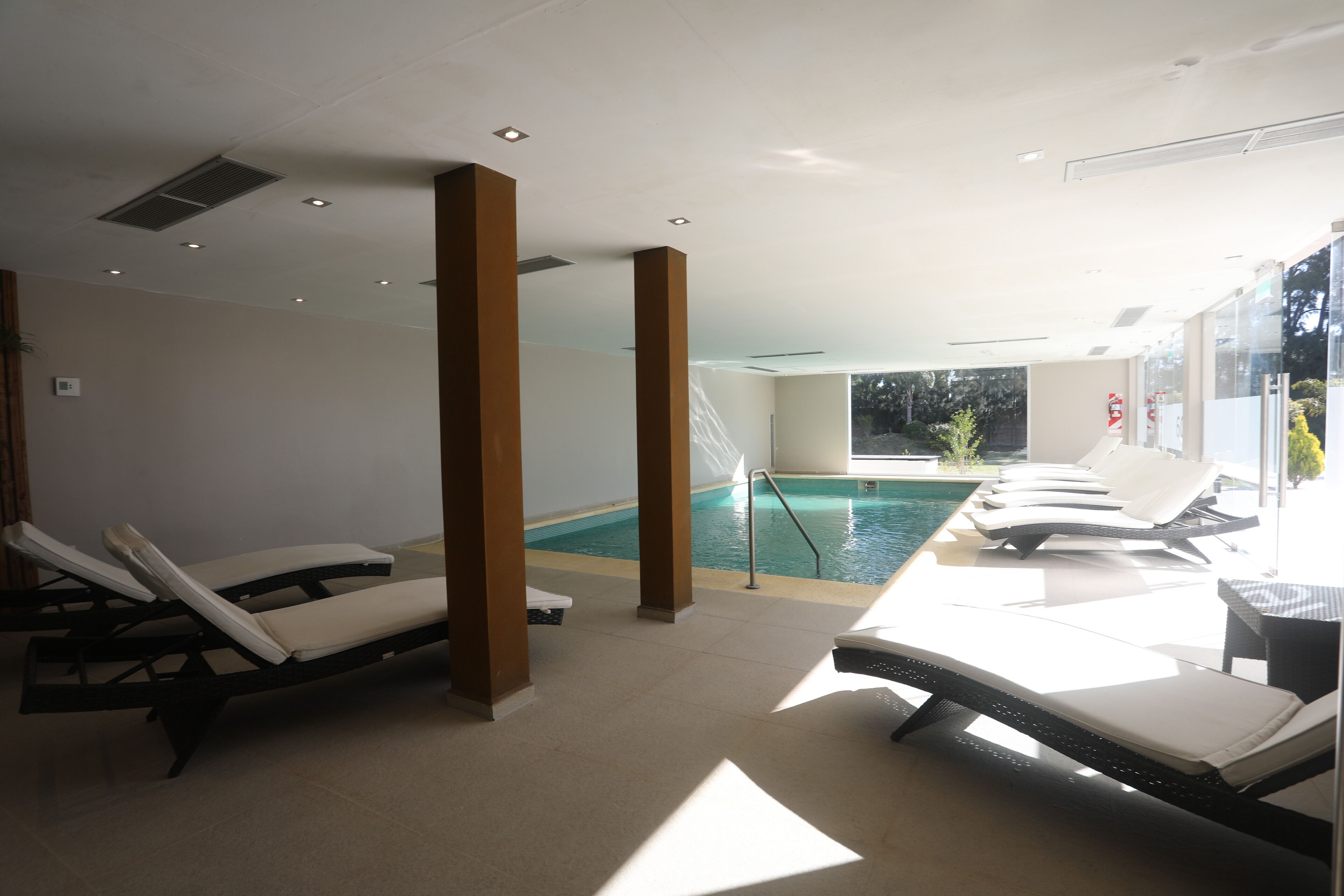 A sunlit indoor pool area with lounge chairs and a view of the outdoor pool.
