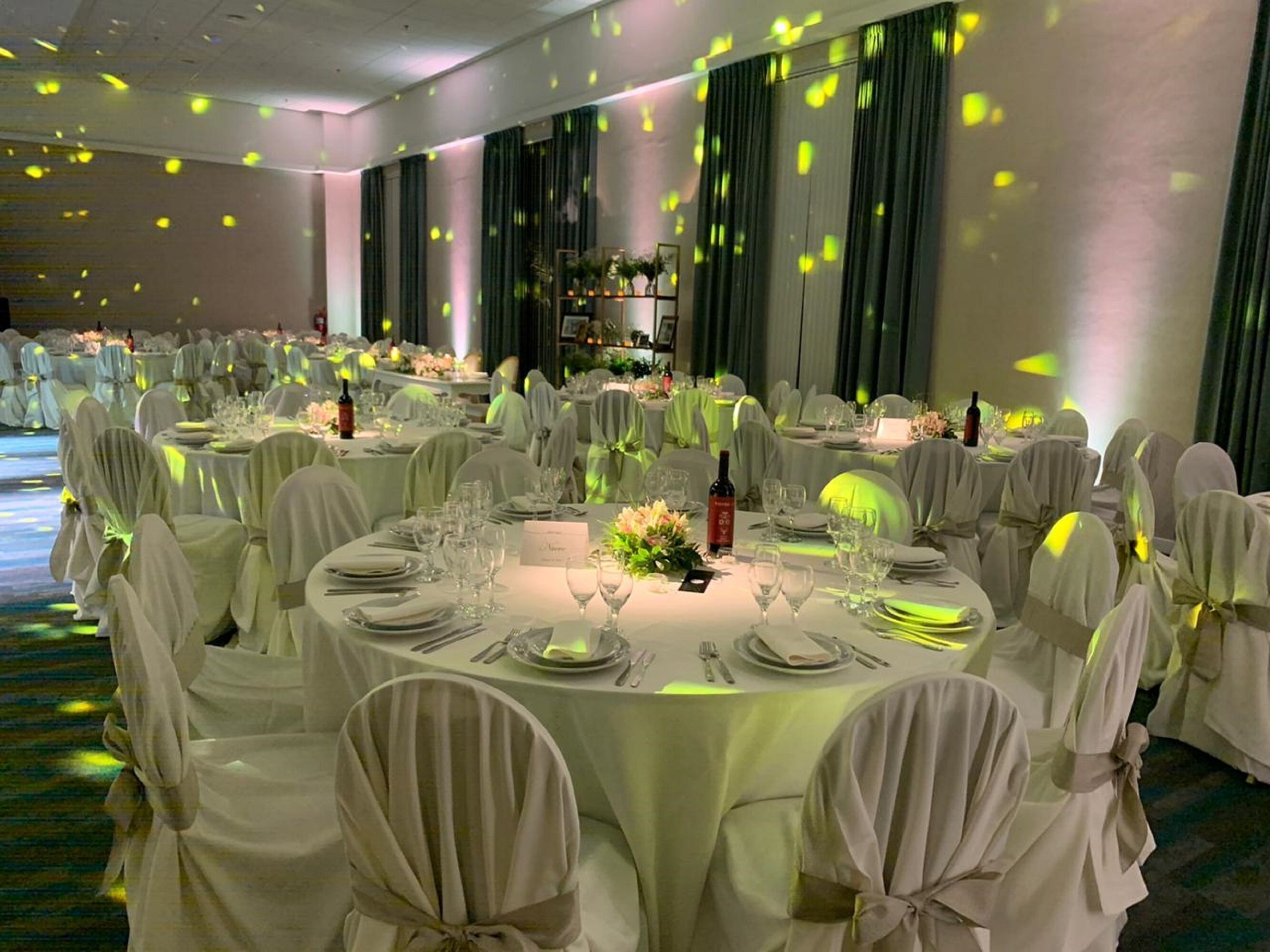 Uma sala de banquetes com mesas redondas dispostas para um evento formal, incluindo cadeiras, louças e um arranjo floral central.