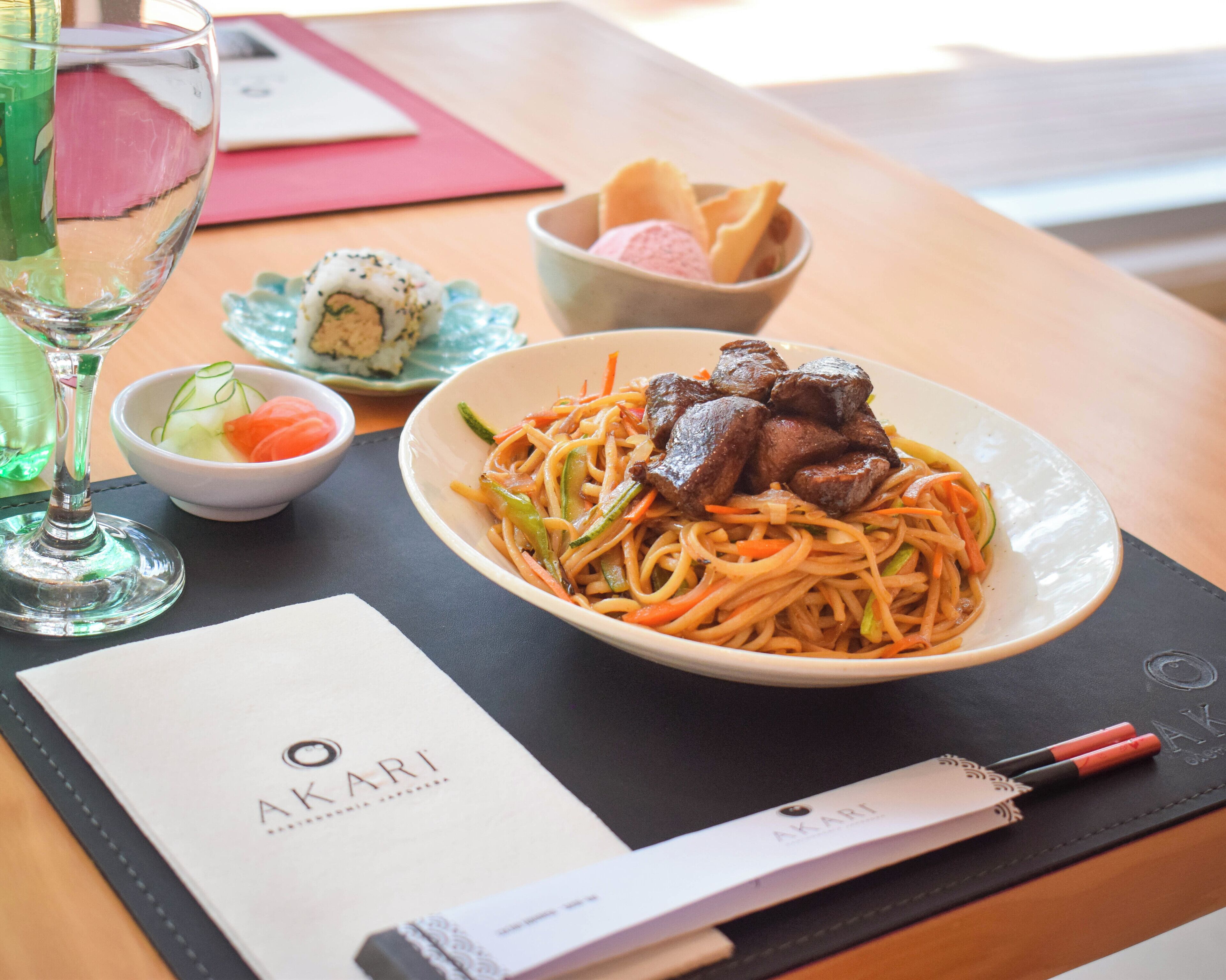 A bowl of noodles with meat, a glass of green drink, and a menu on a table.