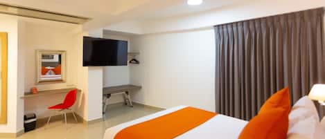 Una habitación de hotel con una cama, un escritorio con silla, un televisor y una ventana con cortinas.