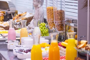 Un bufé con diferentes opciones de comida y bebidas, como frutas, cereales y jugos.