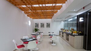 Un espace repas moderne avec des chaises blanches et rouges, un long comptoir proposant une variété de plats, et une structure de plafond en bois.