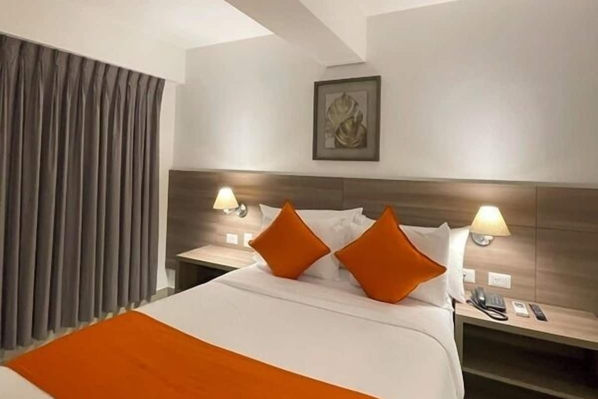 Une chambre d’hôtel avec un grand lit, deux tables de chevet avec des lampes, une tête de lit et un tableau encadré au mur.