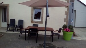 An outdoor patio with a table and chairs, a brown umbrella, and a green potted plant. - House in the countryside 10 minutes from beautiful sandy beaches, ideal for visits (cast)