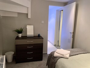 A bedroom with a bed, a dresser with drawers, a mirror, a potted plant, and a door leading to another room. - Richmond House by Staytor (Exeter)