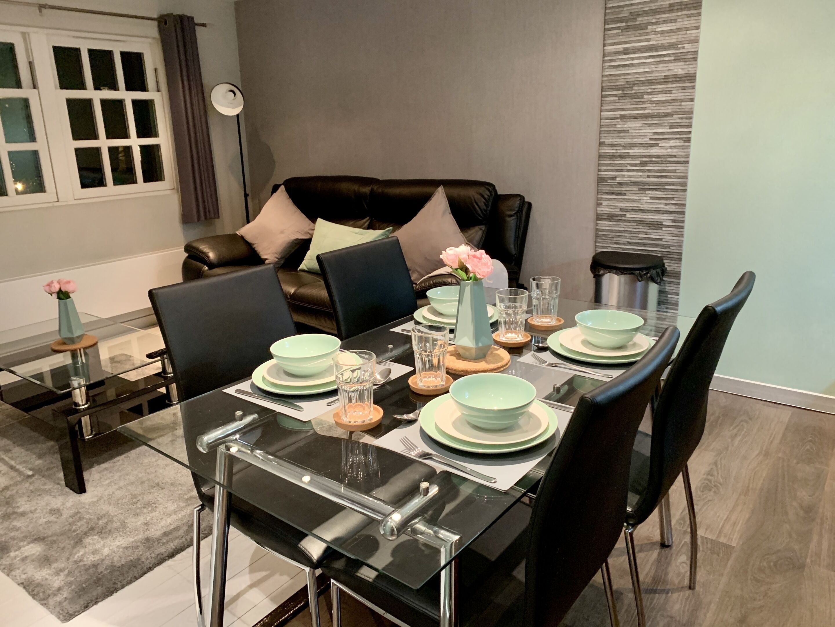 A dining area with a glass table set for four, surrounded by black chairs.