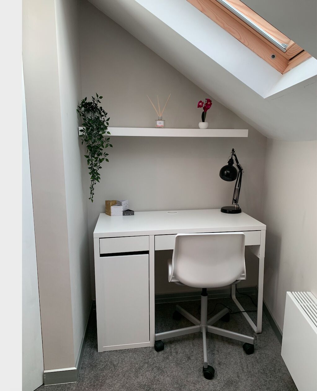 A compact office space with a white desk, a black desk lamp, a white chair, a small potted plant, and a shelf with decorative items.