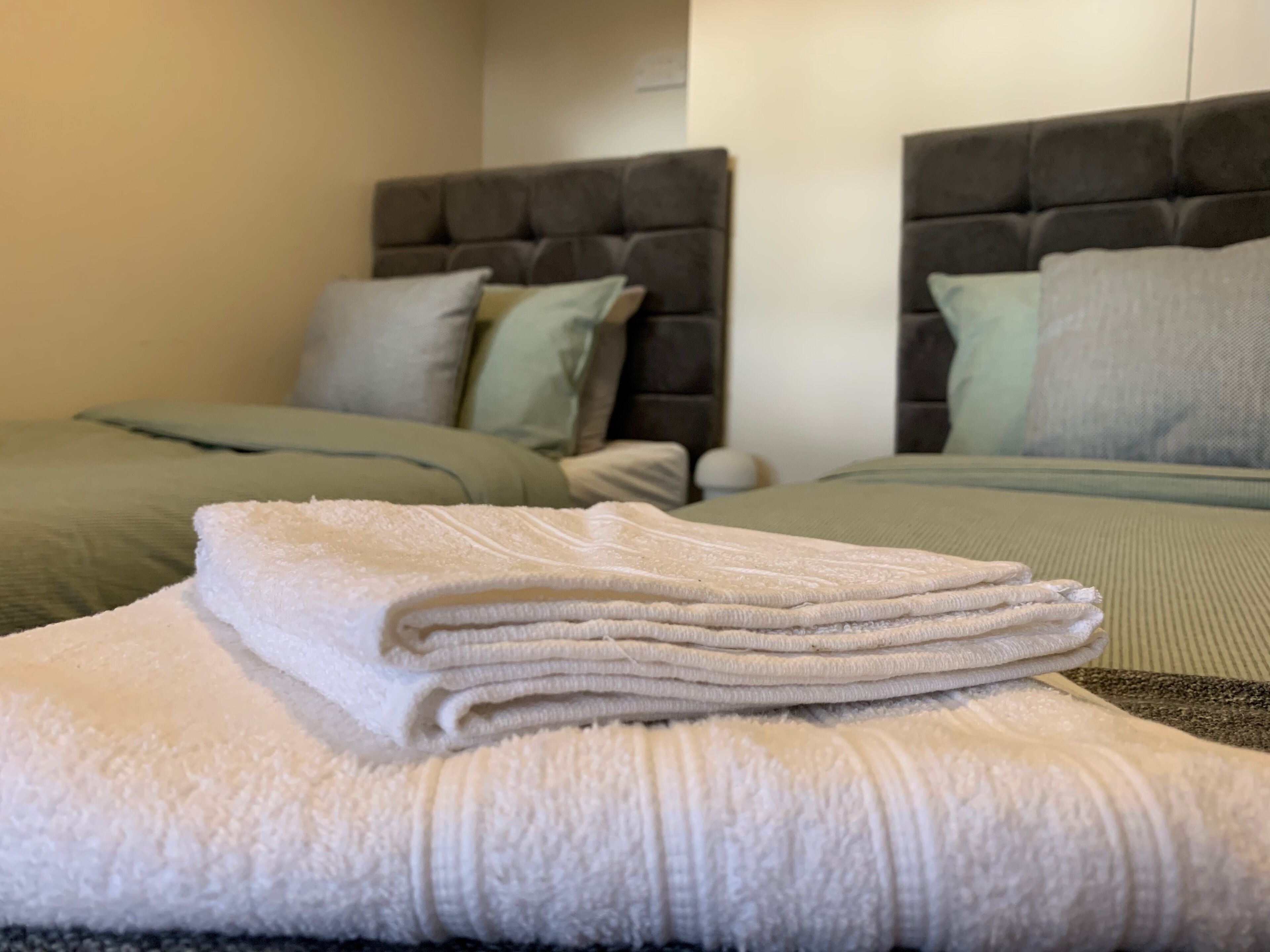 A neatly made bed with a folded white towel on top, a grey headboard, and a green bedspread.