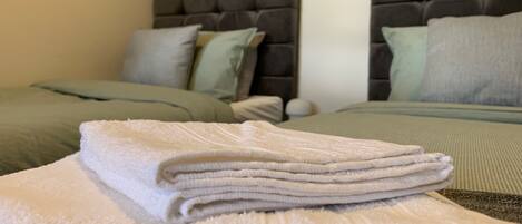 A neatly made bed with a folded white towel on top, a grey headboard, and a green bedspread.