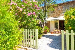 A garden with a gravel path leading to a building with a white door and a small patio area with chairs and a table.