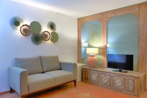 A living room with a sofa, a television on a wooden cabinet, decorative wall art, and a lamp.