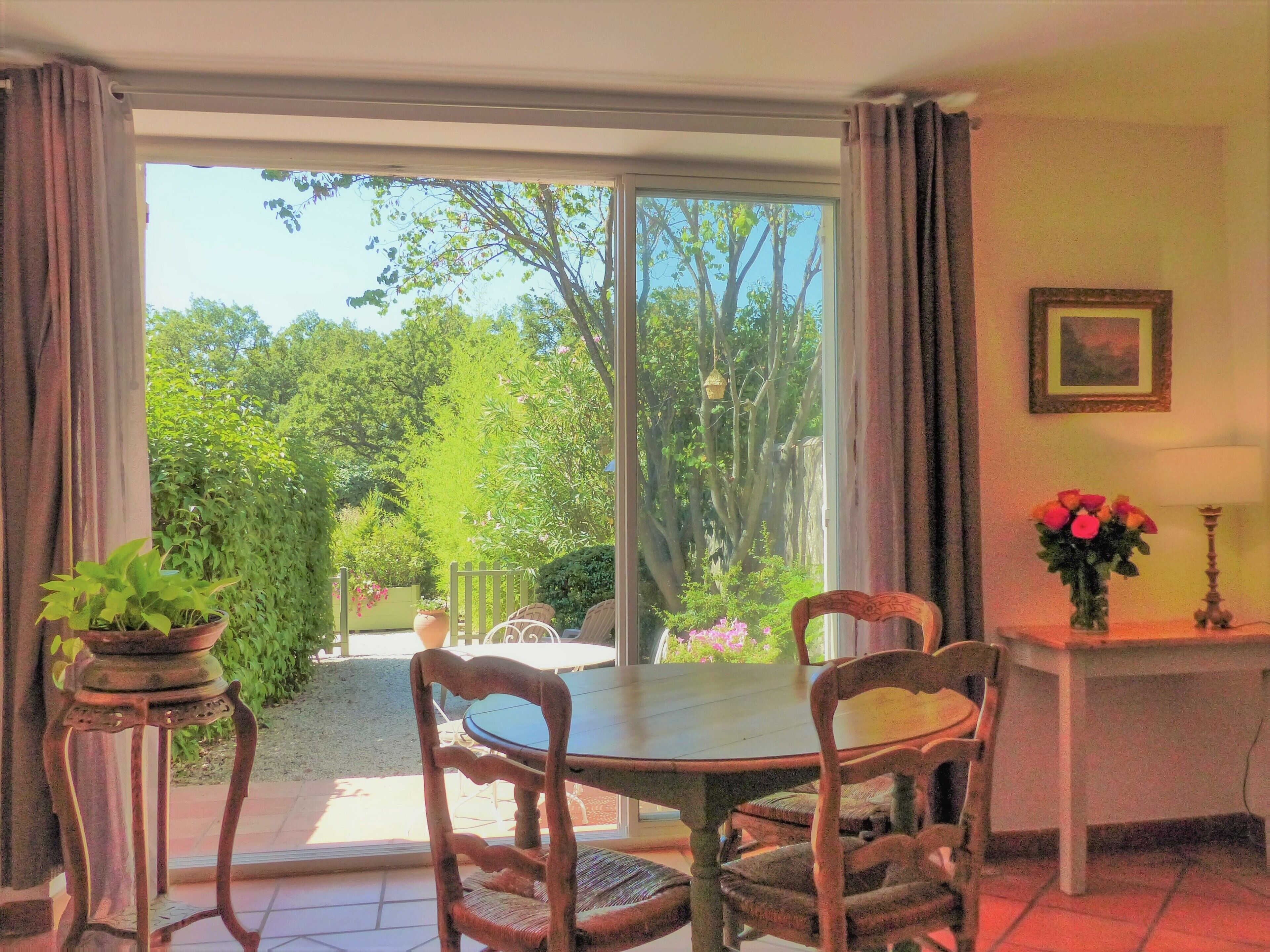 A dining area with a table and chairs, a potted plant, a vase with flowers, and a framed picture on the wall.